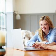 Two adults seated at a wooden table working together on a laptop in a bright, modern workspace with large windows and soft natural light.