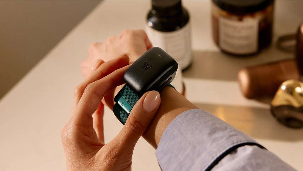 Person adjusting a Whoop fitness tracker on their wrist, with the screenless wearable device and band visible on a tabletop background.