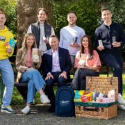 Group of Homegrown at Maxol 2026 winners and Maxol CEO seated and standing outdoors in a park, holding Oatco Super Bites, Well. Can&rsquo;d Water cans and WONDR Jellies, with branded picnic hamper and products displayed in front.