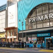 Crowds outside the Primark flagship store at Herald Square in Manhattan, showing the large blue storefront with Primark signage, surrounding retail buildings, and people queuing along the street.
