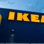 IKEA store exterior with large illuminated yellow IKEA sign mounted on a dark blue facade at Gateway Retail Park, photographed from a low angle against a cloudy sky.