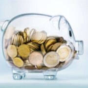 Glass piggy bank filled with euro coins on a light background, symbolising savings, wages, or salary transparency in employment.