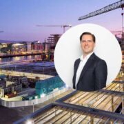 Urban construction site at dusk with multiple cranes over new office and apartment buildings beside a river; circular inset shows a business executive in a suit.