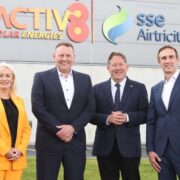 Four people stand outdoors in front of a modern commercial building with Activ8 Solar Energies and SSE Airtricity logos displayed on the wall, marking the launch of a funded solar initiative.