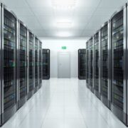 Rows of glass-fronted server racks inside a modern data centre, with illuminated network equipment lining both sides of a clean, brightly lit corridor.