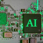 Close-up of a microchip on a circuit board illuminated in green light, with the letters AI displayed on the central processor and interconnected electronic components surrounding it.
