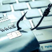 Close-up of a credit card on a computer keyboard being hooked by a fishing hook, symbolising online payment fraud and phishing attacks targeting banking customers.