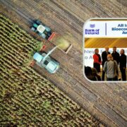 Aerial view of a harvester working in a crop field, collecting agricultural material, with an inset image showing an awards presentation at the All Island Bioeconomy Awards 2026 sponsored by Bank of Ireland.