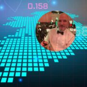 Business-themed graphic showing a digital stock market background with glowing data points, charts and numerical indicators, featuring a circular inset photo of a person dressed in formal attire holding an award at an indoor event, positioned over a stylised global or financial data grid backdrop in blue and teal tones.