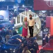 Crowded electric vehicle show floor featuring multiple EV models and brand stands, with attendees browsing; inset shows two people standing in a bright indoor setting.