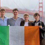 Four young founders stand side by side holding an Irish tricolour flag with the Golden Gate Bridge visible in the background in San Francisco.
