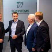 Four business professionals in conversation at the SE Systems office in Ireland, standing beneath the company logo during a corporate meeting focused on sustainability, engineering, and energy solutions.