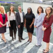 Group photo of six professionals standing in a bright modern office atrium with glass walls and natural light, marking the graduation of the inaugural NOVA Women in Tech Leadership Programme run by Technology Ireland Digital Skillnet and Connecting Women in Technology (CWiT).