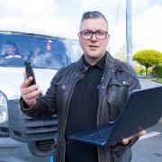 Business owner using a smartphone and laptop in front of a delivery van, illustrating the VanQuotes.ie platform connecting customers with man-with-a-van and transport services across Ireland.