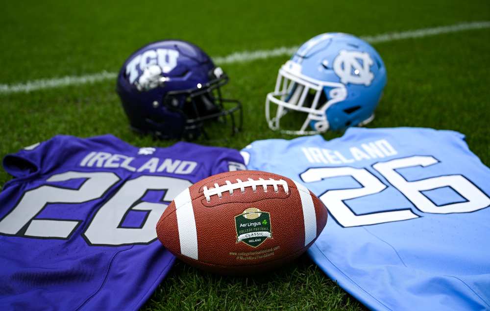 American football featuring the Aer Lingus College Football Classic logo positioned between TCU Horned Frogs and North Carolina Tar Heels jerseys and helmets on a grass pitch ahead of the Dublin college football game.