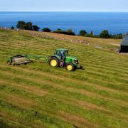 Tractor harvesting silage on an Irish farm overlooking the coast, highlighting agriculture, agritech innovation and the Irish farming sector.