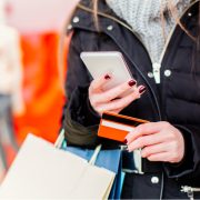 Person using a smartphone while holding a payment card and shopping bags, illustrating Lidl Connect mobile services in Ireland.
