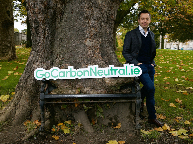 Man standing beside a tree with a sign saying Gocarbonneutral.ie.