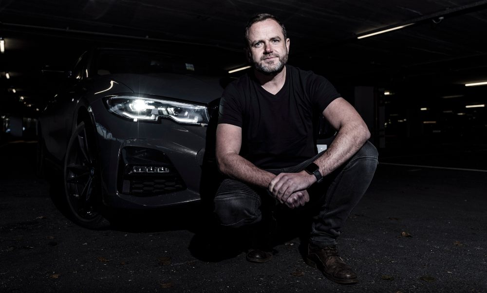 Man on knee in front of a car.