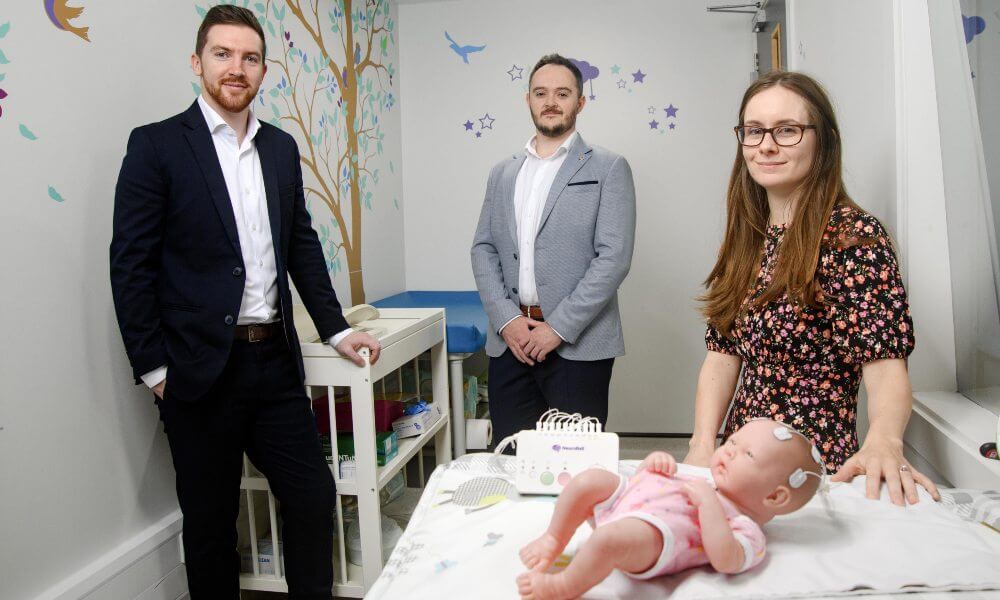 Two men and a woman demonstrating medtech for newborn babies.
