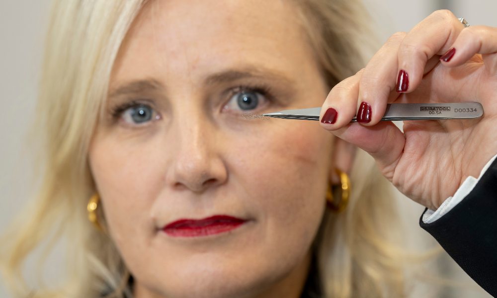 Woman holding tiny medical stent device between a tweezers.