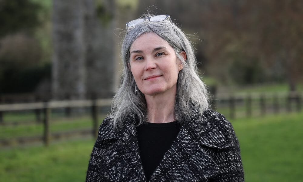 Woman in checkered coat standing in a field.