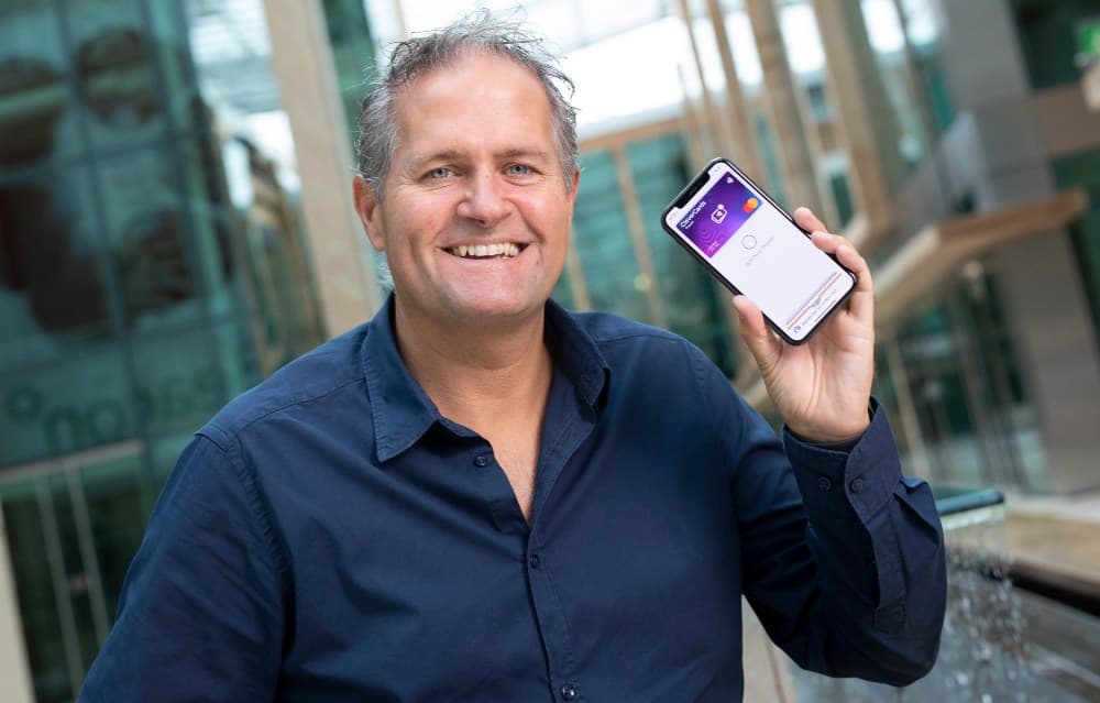 Smiling man in navy-blue shirt holding phone.