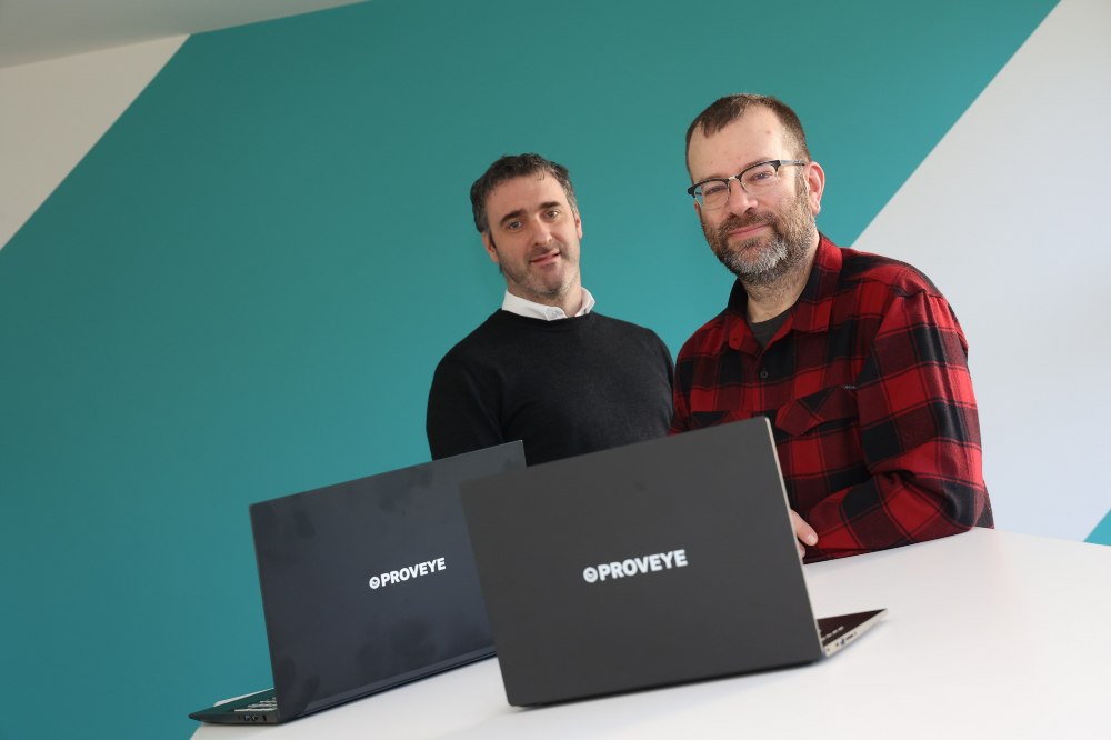Two men standing behind two laptop computers.